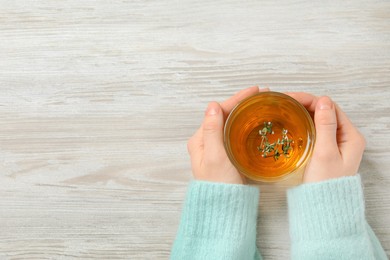 Photo of Woman holding cup of tasty herbal tea with thyme at white wooden table, closeup. Space for text