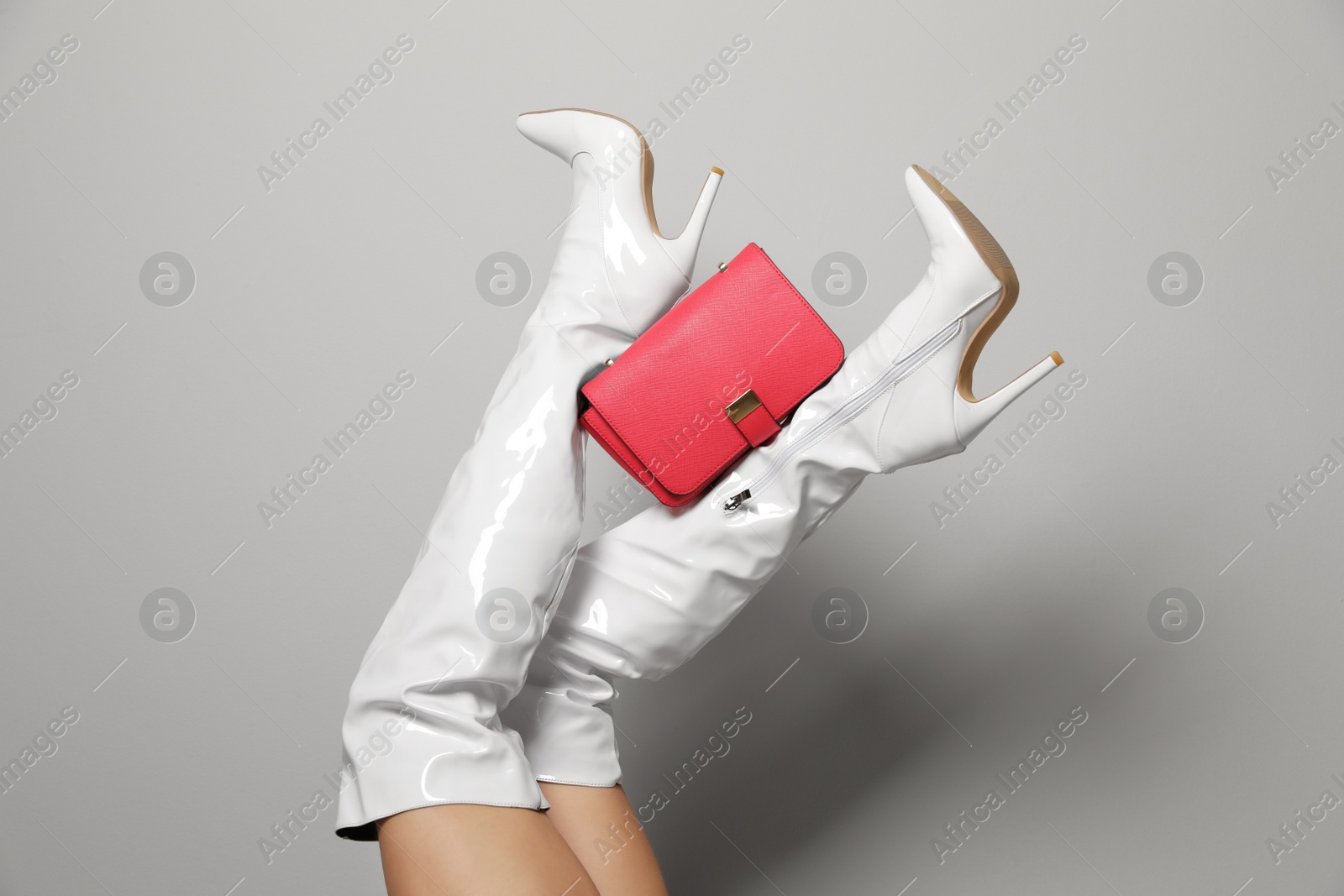 Photo of Woman wearing white long shoes with red leather bag on light background, closeup