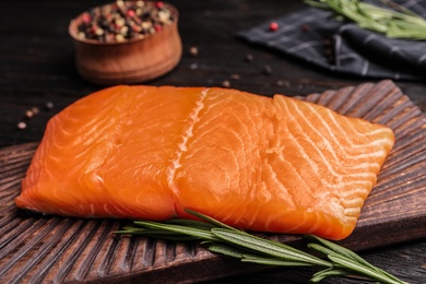 Photo of Wooden board with tasty salmon fillet on dark table, closeup