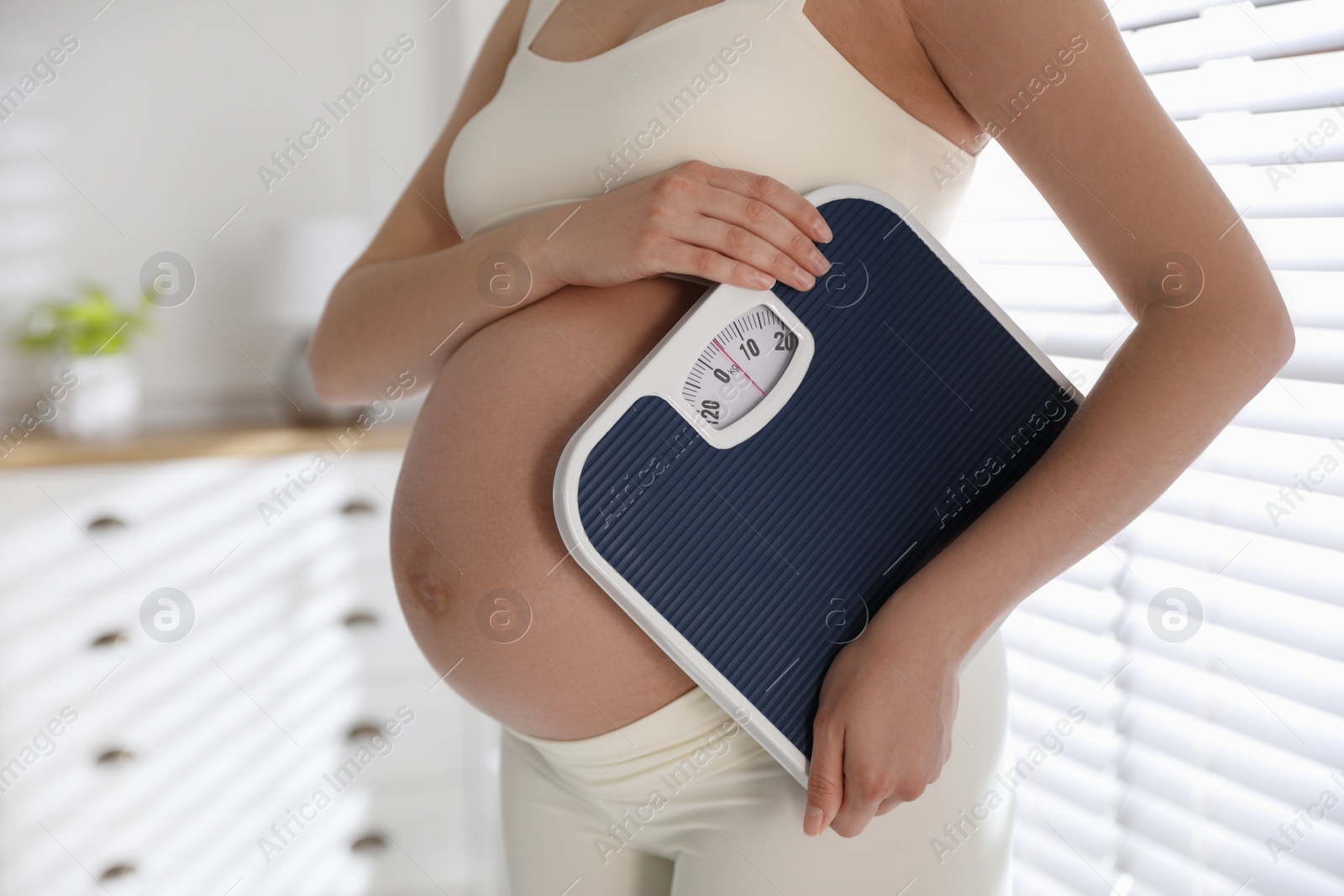 Photo of Young pregnant woman with scales at home, closeup