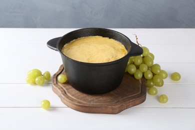 Photo of Fondue with tasty melted cheese and grapes on white wooden table