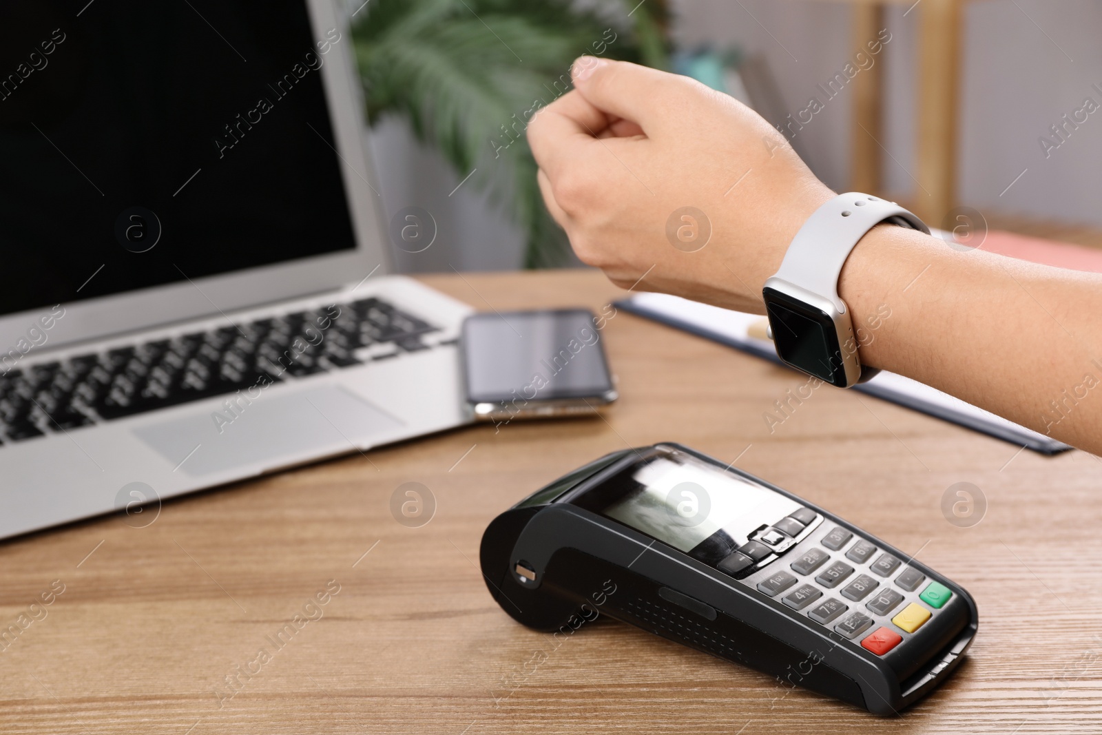 Photo of Woman using terminal for contactless payment with smart watch at table