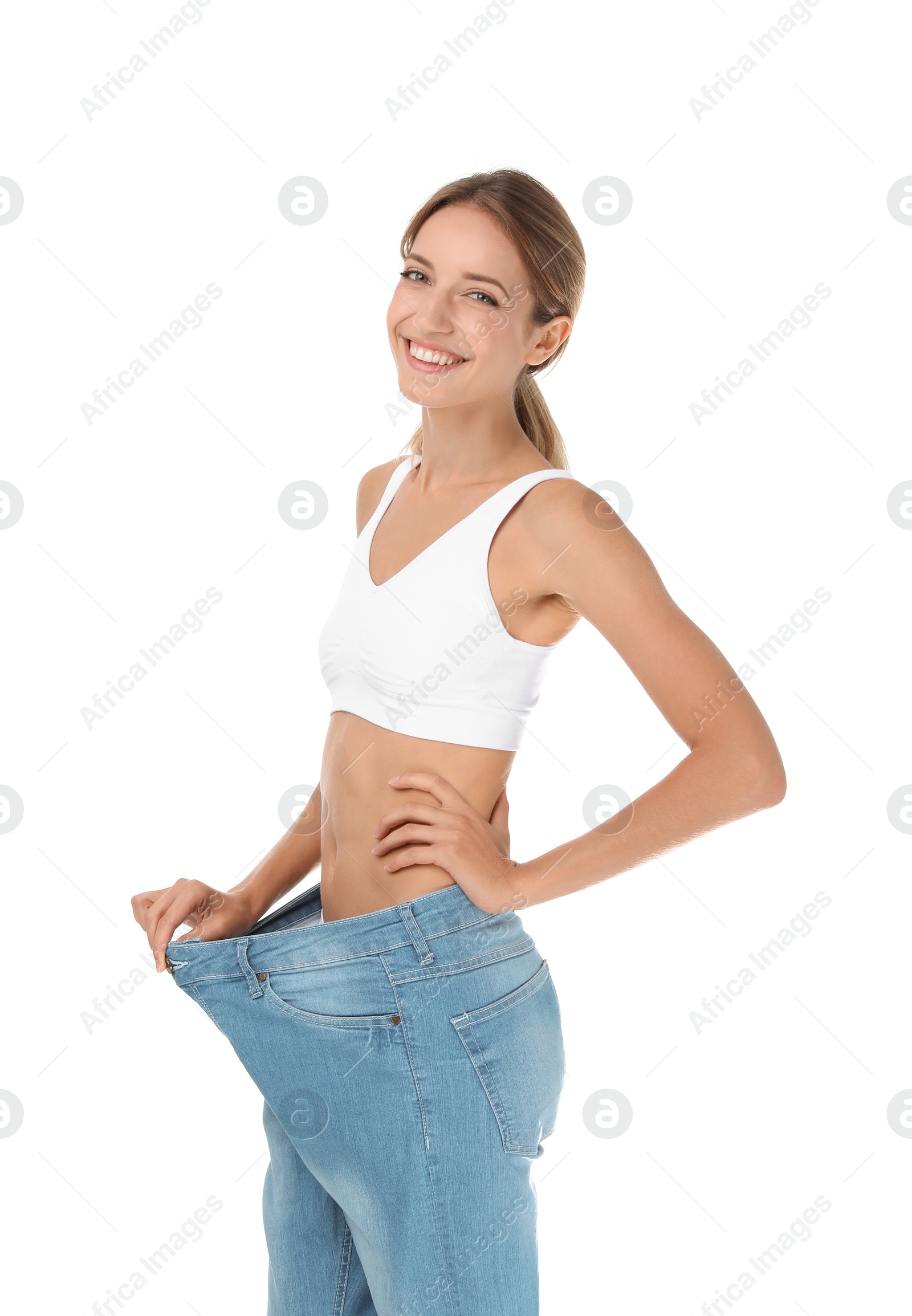 Photo of Young slim woman in old big jeans showing her diet results on white background