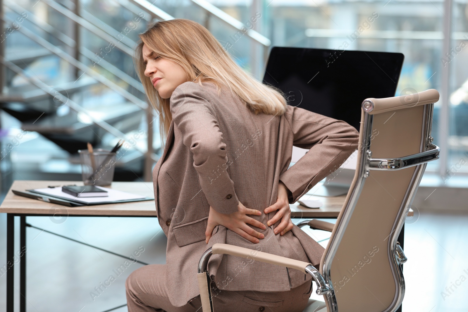 Photo of Young woman suffering from back pain in office