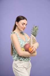 Woman with string bag of fresh fruits on violet background
