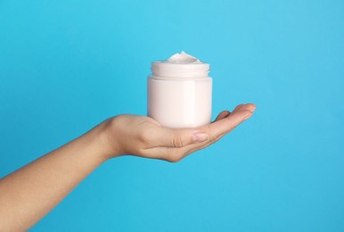 Photo of Woman holding jar of face cream on light blue background, closeup