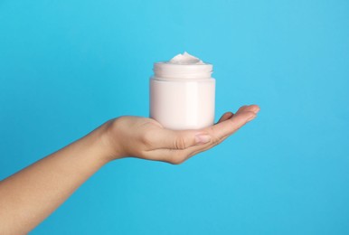 Woman holding jar of face cream on light blue background, closeup