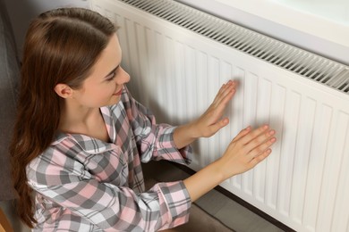 Photo of Woman warming hands on heating radiator near white wall