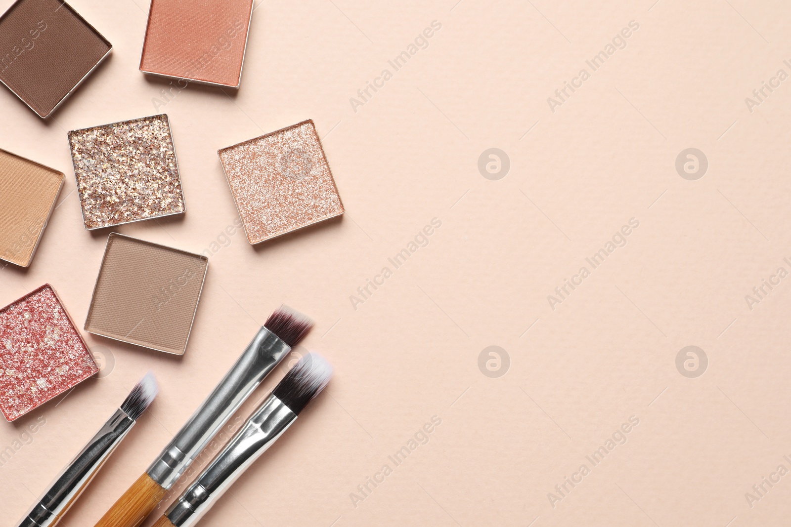 Photo of Different beautiful eye shadows and makeup brushes on beige background, flat lay. Space for text