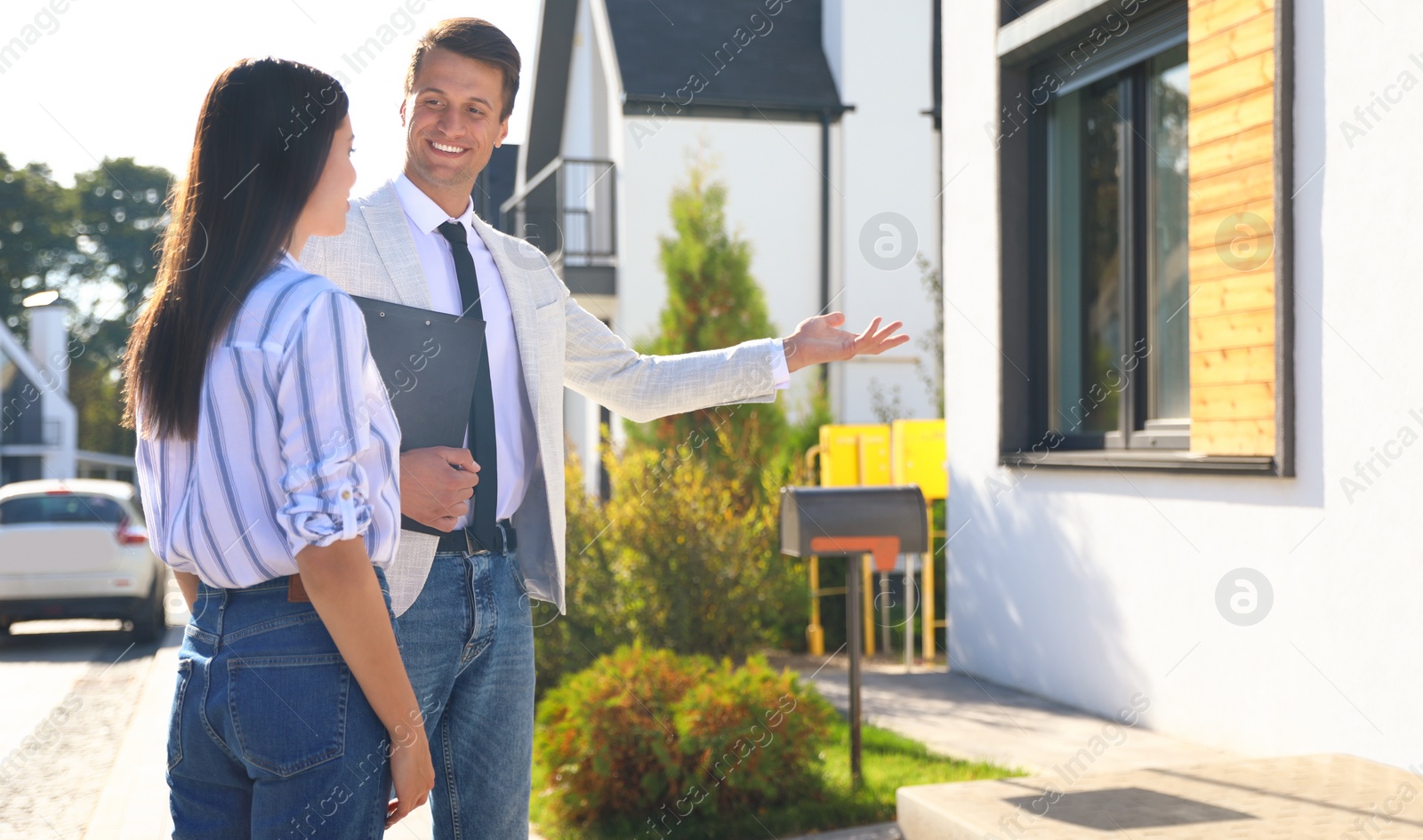 Photo of Real estate agent showing house to young woman outdoors