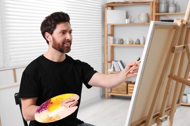 Photo of Happy man painting in studio. Using easel to hold canvas