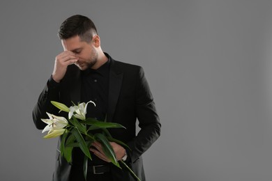 Sad man with white lilies mourning on grey background, space for text. Funeral ceremony