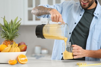 Photo of Man pouring tasty smoothie into glass at white marble table in kitchen, closeup