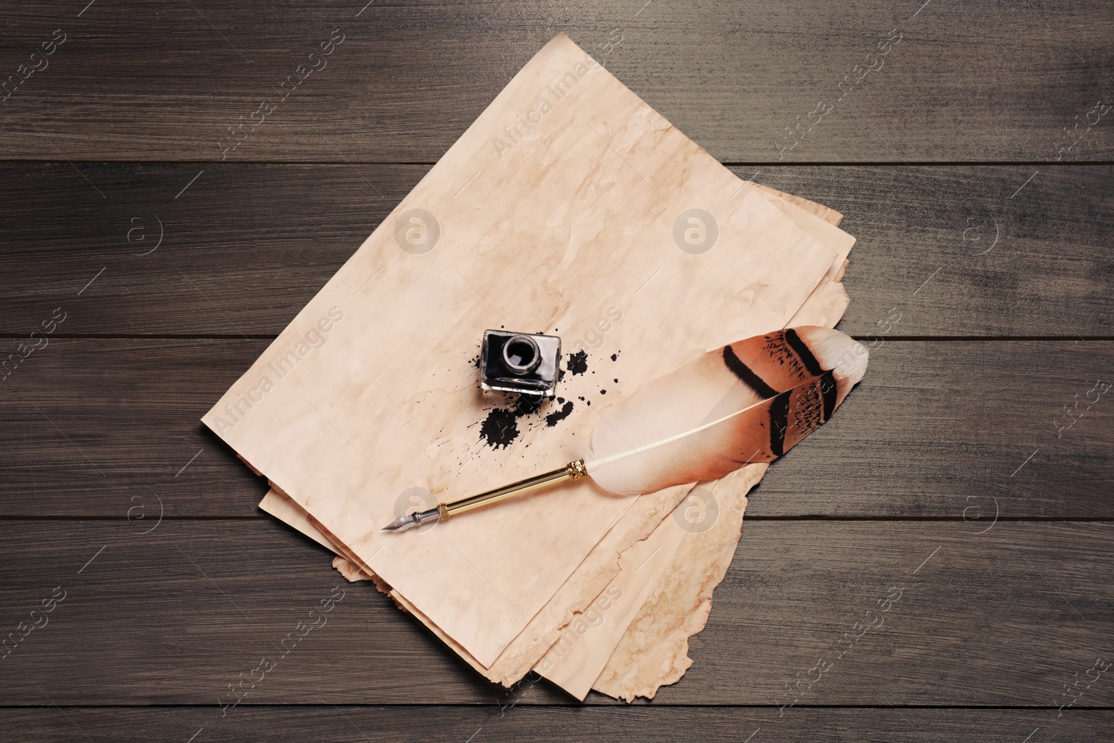 Photo of Feather pen, inkwell and vintage parchment with ink stains on wooden table, top view