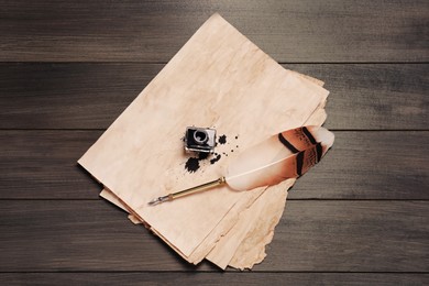 Feather pen, inkwell and vintage parchment with ink stains on wooden table, top view