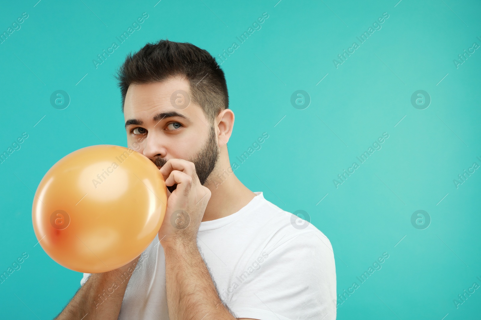 Photo of Man inflating bright balloon on turquoise background, space for text
