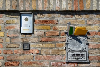 Photo of Vintage post box with newspaper and letter near modern intercom on old brick wall