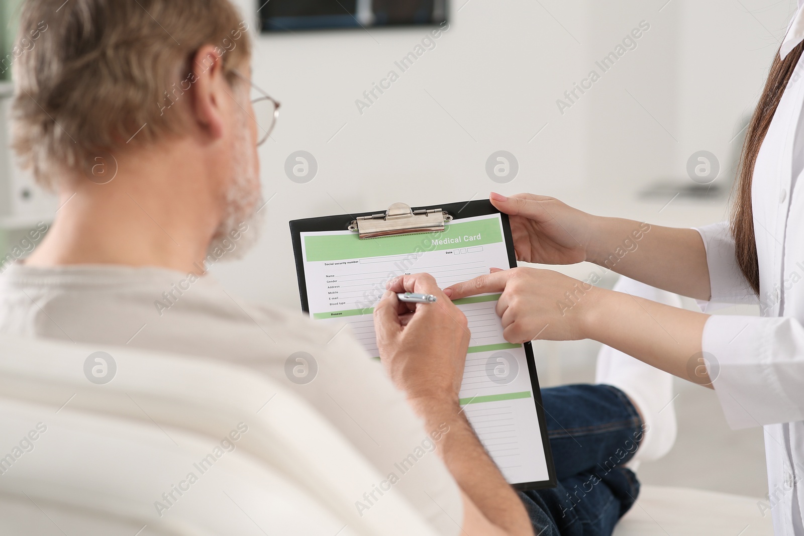 Photo of Doctor helping patient filling his medical card in clinic, closeup