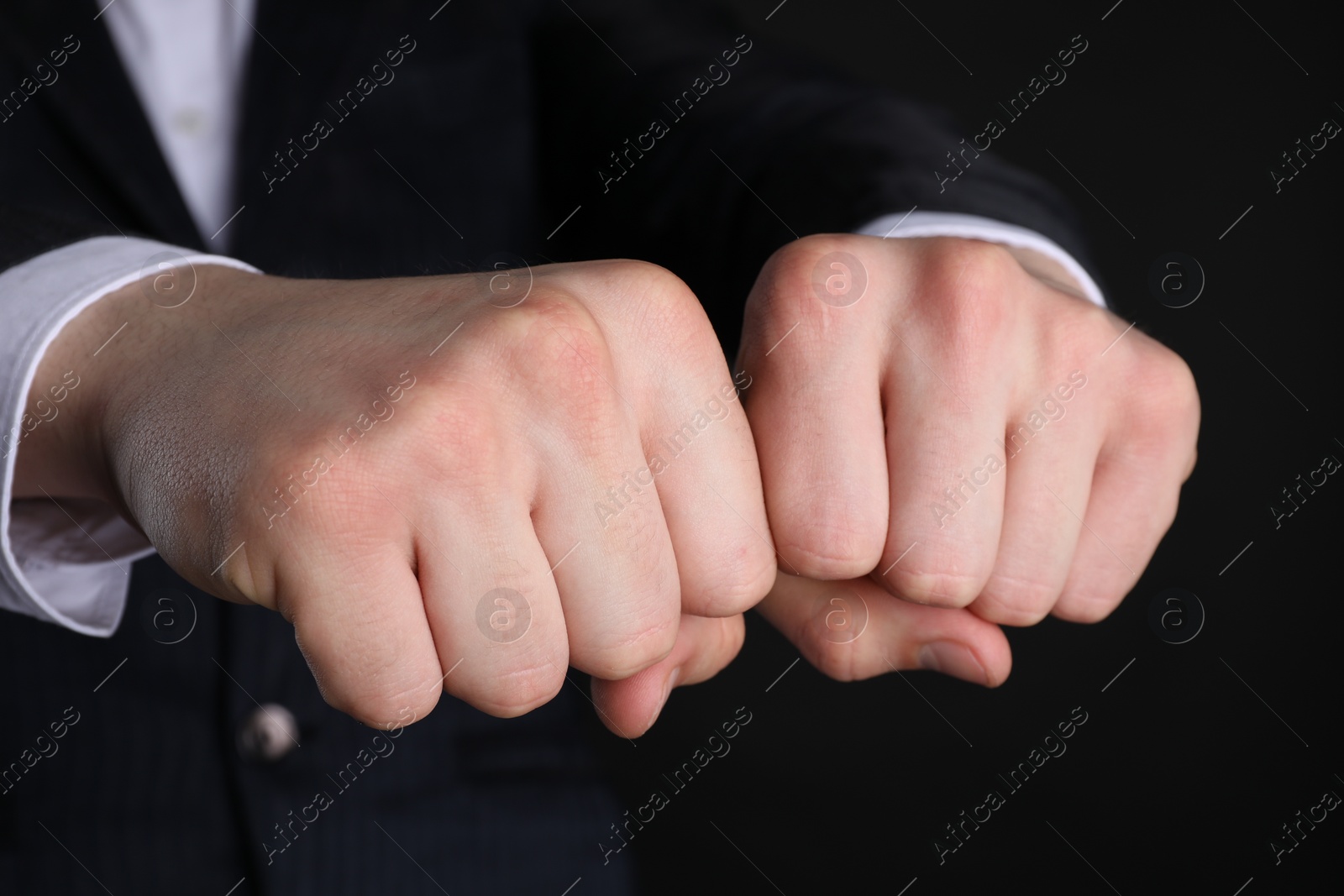 Photo of Businessman showing fists with space for tattoo on black background, closeup