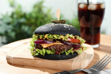 Board with black burger served on wooden table