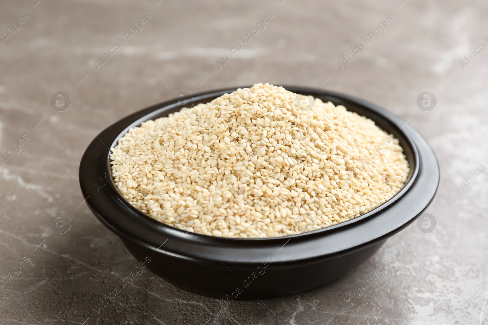 Photo of Sesame seeds in bowl on grey marble table