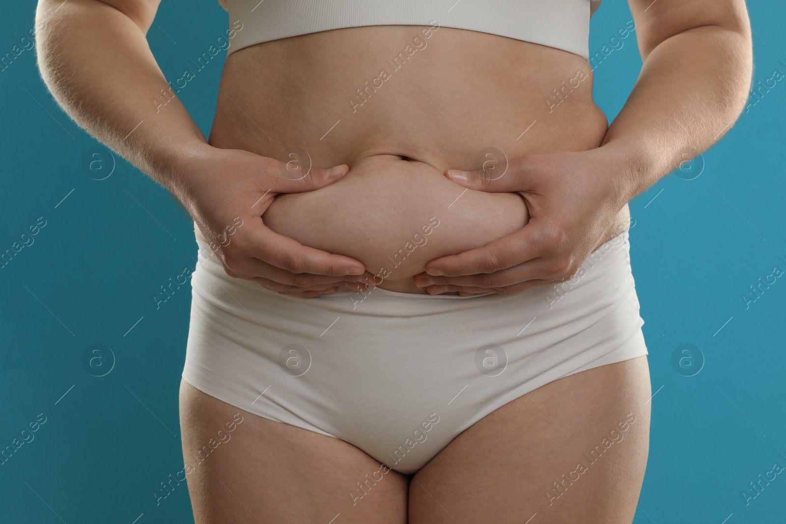 Photo of Woman touching belly fat on light blue background, closeup. Overweight problem