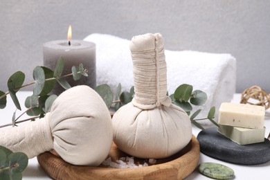 Spa composition with herbal massage bags and eucalyptus branches on white table