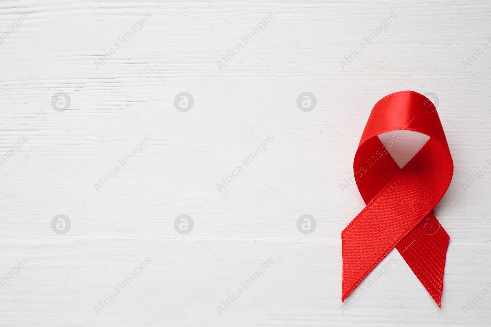 Photo of Top view of red ribbon on white wooden background, space for text. AIDS disease awareness