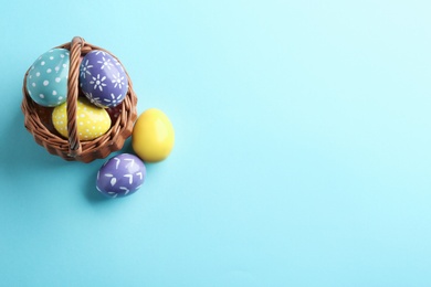 Wicker basket with painted Easter eggs on color background, top view. Space for text