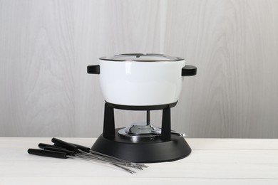 Fondue set on white wooden table. Kitchen equipment