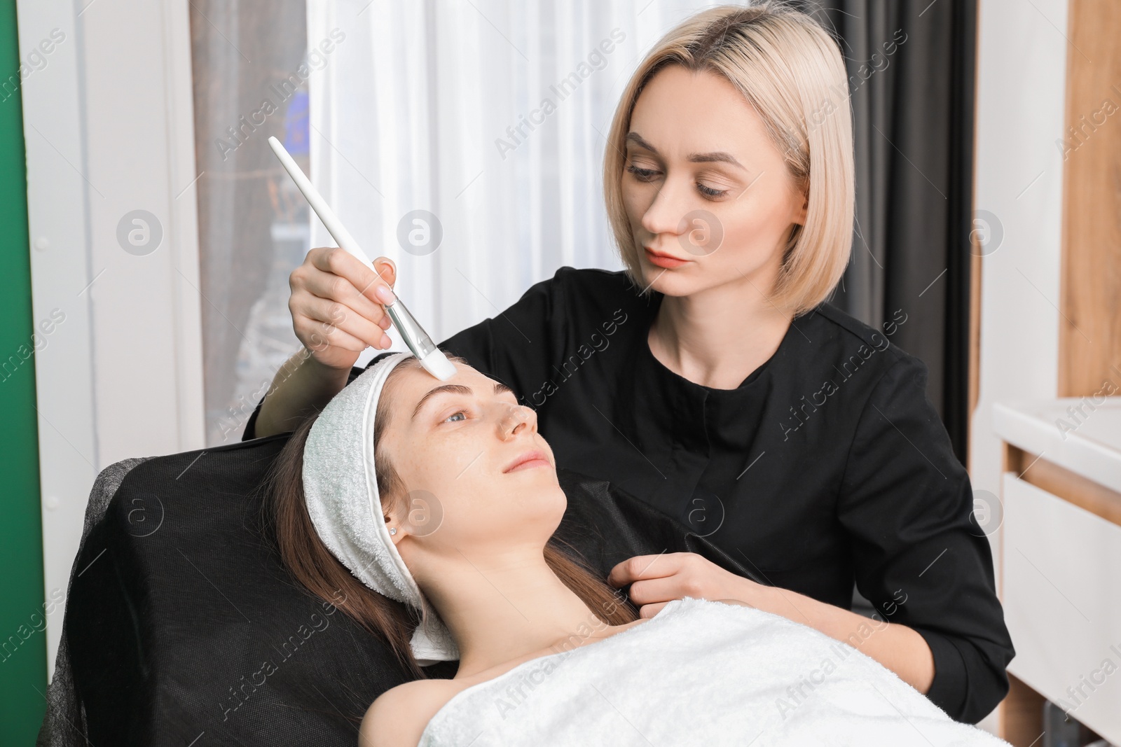 Photo of Cosmetologist applying mask on woman's face in clinic