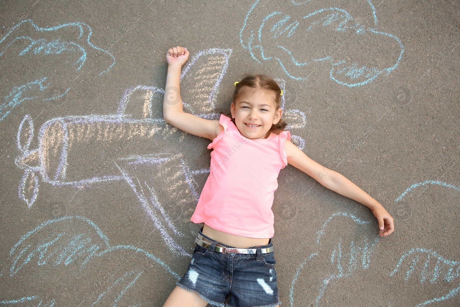 Photo of Little child lying near chalk drawing of airplane on asphalt, top view