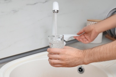 Photo of Man filling glass with water from faucet in kitchen, closeup