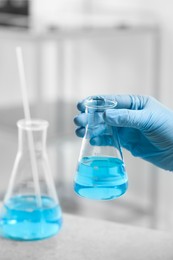 Photo of Scientist holding flask of light blue liquid in laboratory, closeup