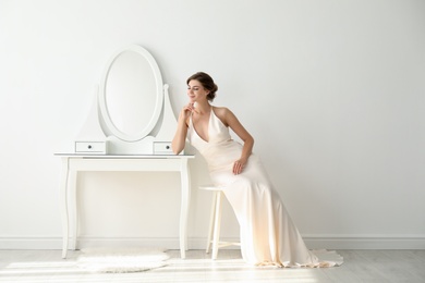 Photo of Young bride in beautiful wedding dress near mirror indoors