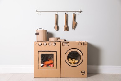 Photo of Cardboard kitchen and washing machine near white wall indoors