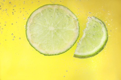 Photo of Juicy lime slices in soda water against yellow background, closeup