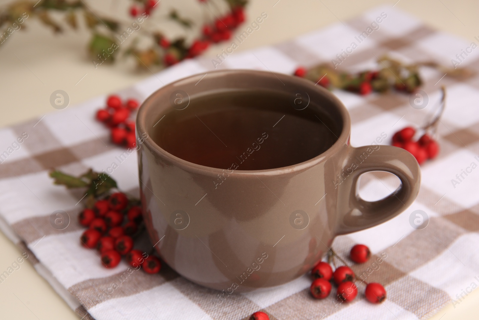 Photo of Brown cup with hawthorn tea and berries on beige table, closeup