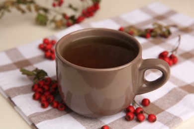 Photo of Brown cup with hawthorn tea and berries on beige table, closeup