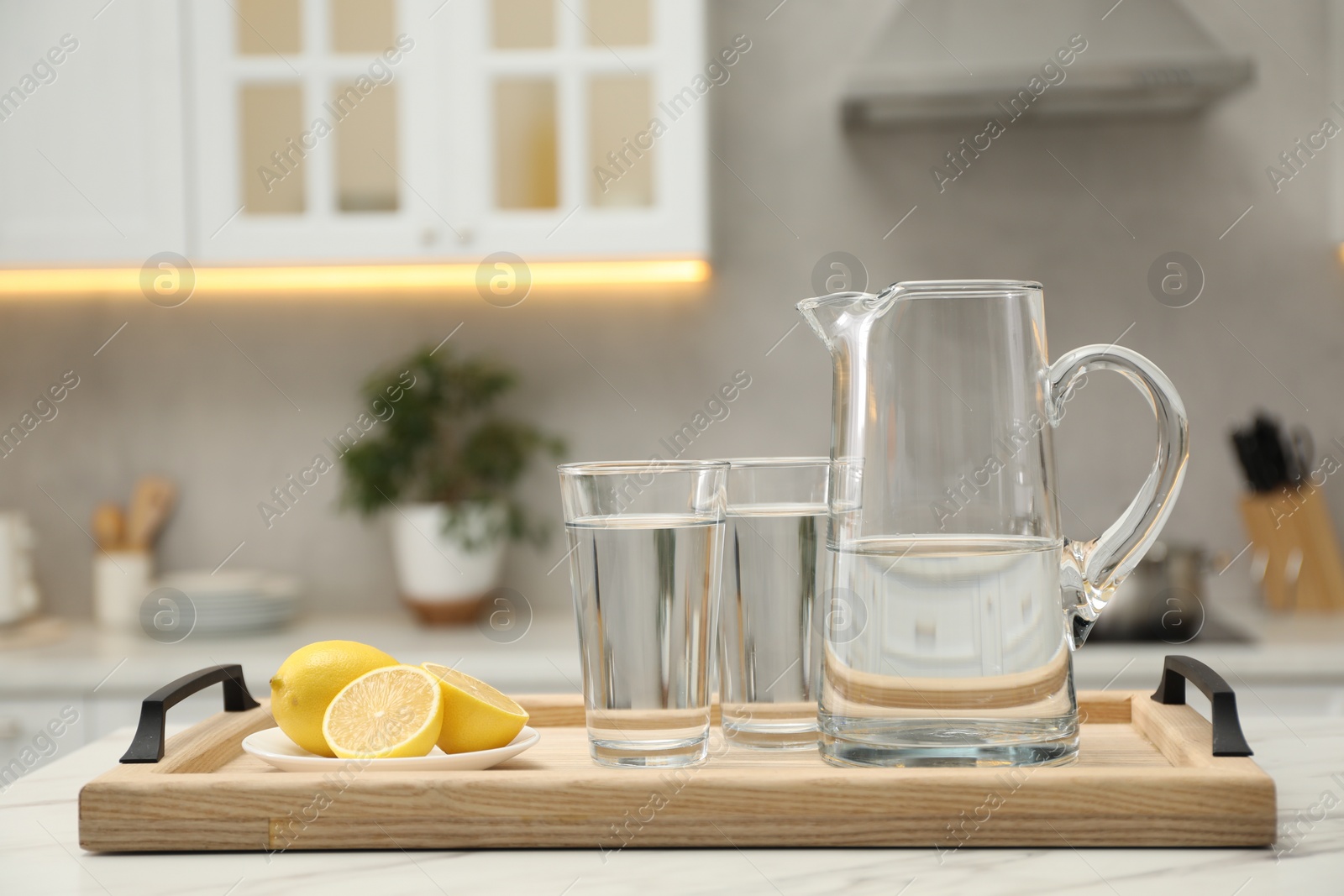 Photo of Jug, glasses with clear water and lemons on white table in kitchen