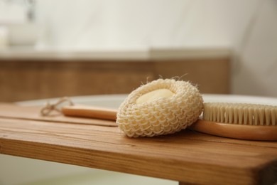 Photo of Wooden bath tray with sponge and brush on tub indoors, closeup