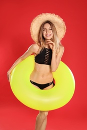 Beautiful young woman in stylish bikini with yellow inflatable ring on red background