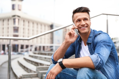 Photo of Portrait of handsome young man talking on phone outdoors. Space for text