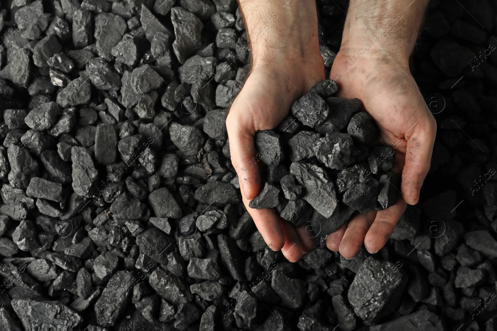 Photo of Man holding coal in hands over pile, top view. Space for text