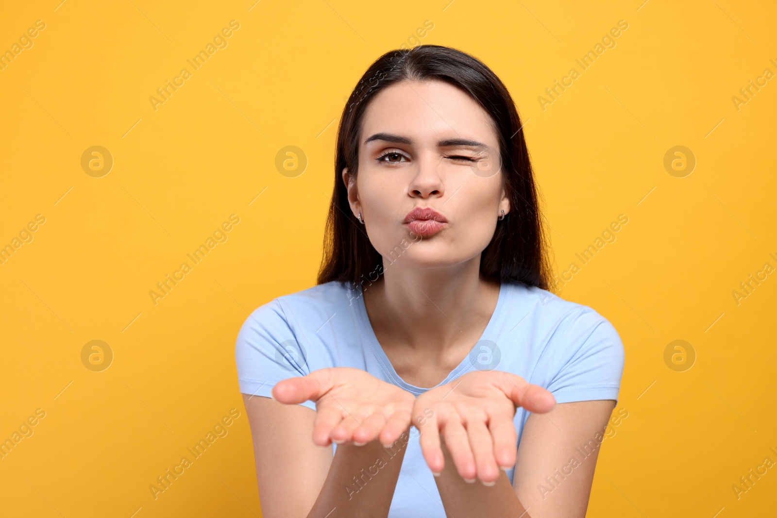 Photo of Beautiful young woman blowing kiss on yellow background