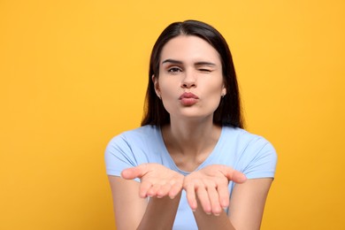 Beautiful young woman blowing kiss on yellow background