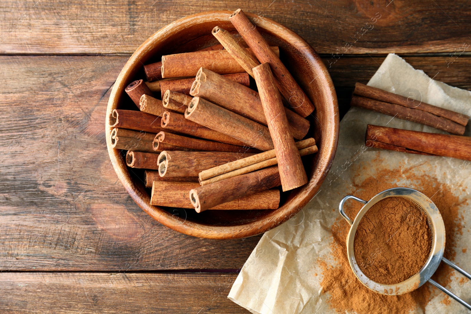 Photo of Bowl with aromatic cinnamon sticks and powder on wooden background