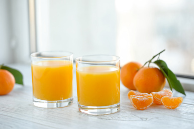 Photo of Glasses of fresh tangerine juice and fruits on white wooden table