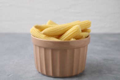 Photo of Tasty fresh yellow baby corns in bowl on grey table, closeup