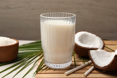 Glass of delicious vegan milk, coconuts and leaf on white wooden table, closeup